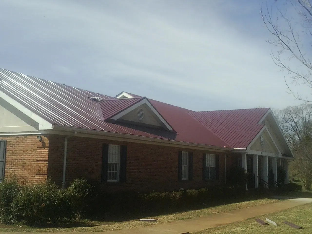 Red metal roof with gabled entries on a long brick building, from a Hail Damage Roof Repair job in Losantville