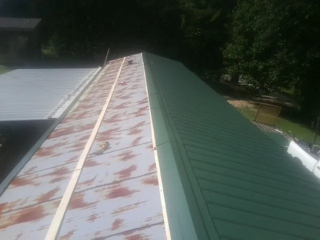 Old rusted panels beside newly installed green metal roofing — Wind Damage Roof Repair by Roofing Brothers in Losantville