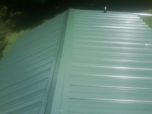 New green metal panels meeting at the ridge of a roof — Flat Roof Repair work by our crew in Losantville