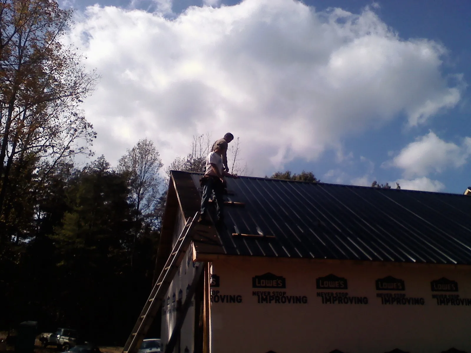 Roofer fastening dark metal panels high against a cloudy sky, from a Roof Inspection job in Losantville