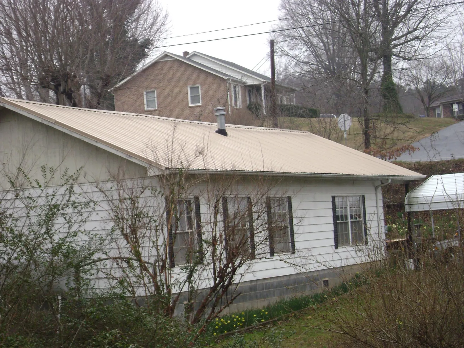 Tan metal roof on a white sided house set into a hillside — Commercial Roofing by Roofing Brothers in Losantville