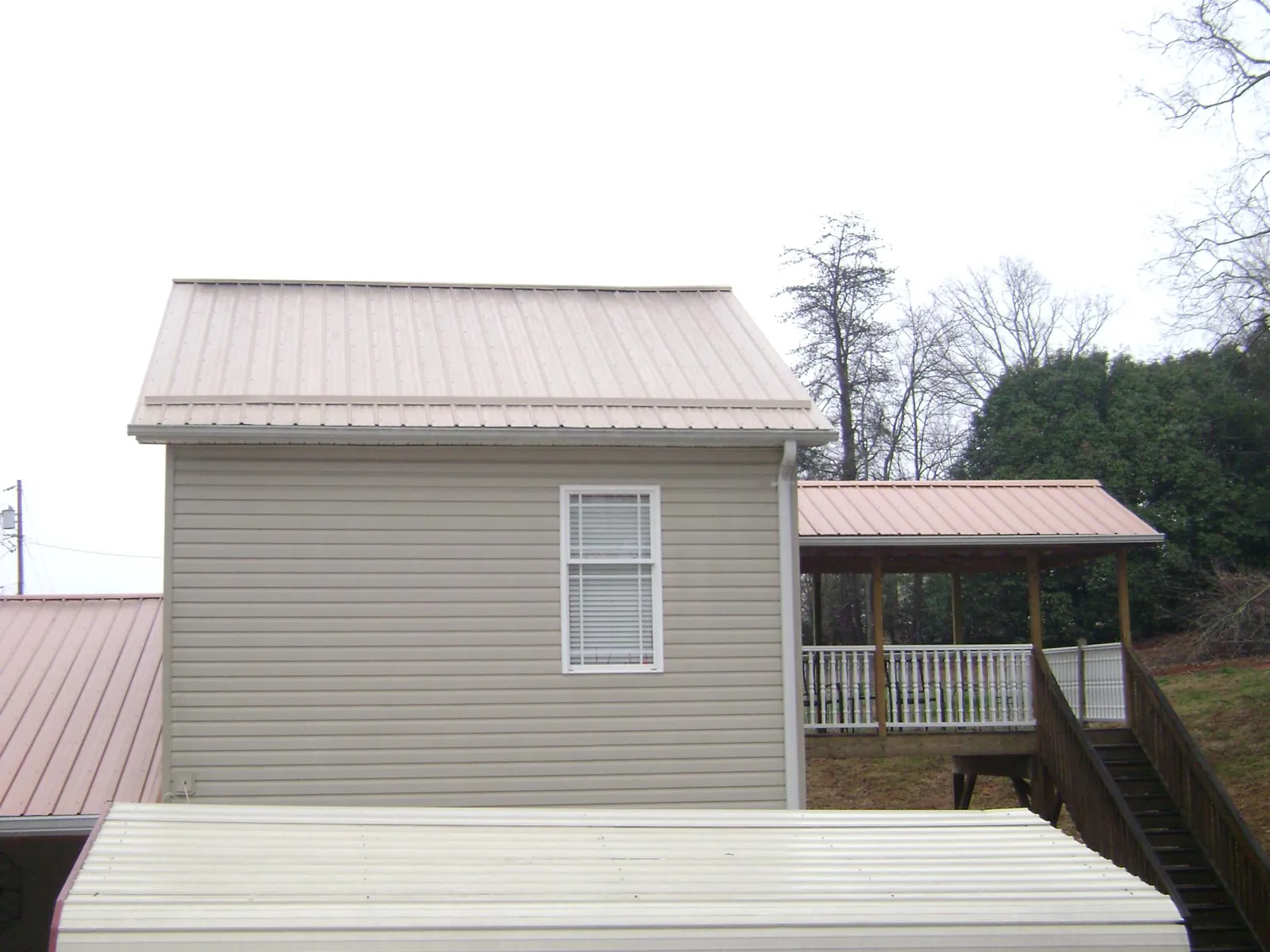 Tan metal roofs on a two story addition and attached porch, from a Roof Replacement job in Losantville